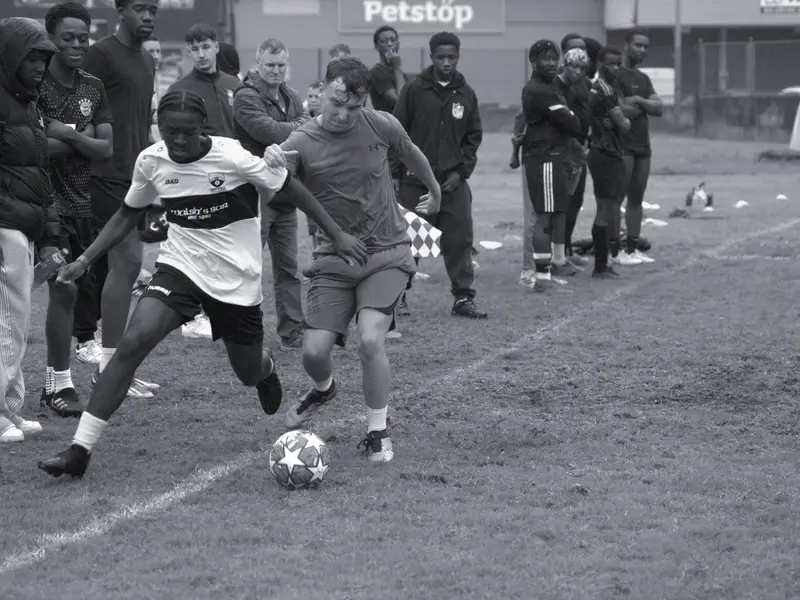 Two players duel for the ball on the touchline in the rain at the 2024 tournament